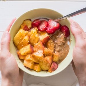 A bowl of cooked rice topped with fruit, nut butter, and a drizzle of maple syrup.
