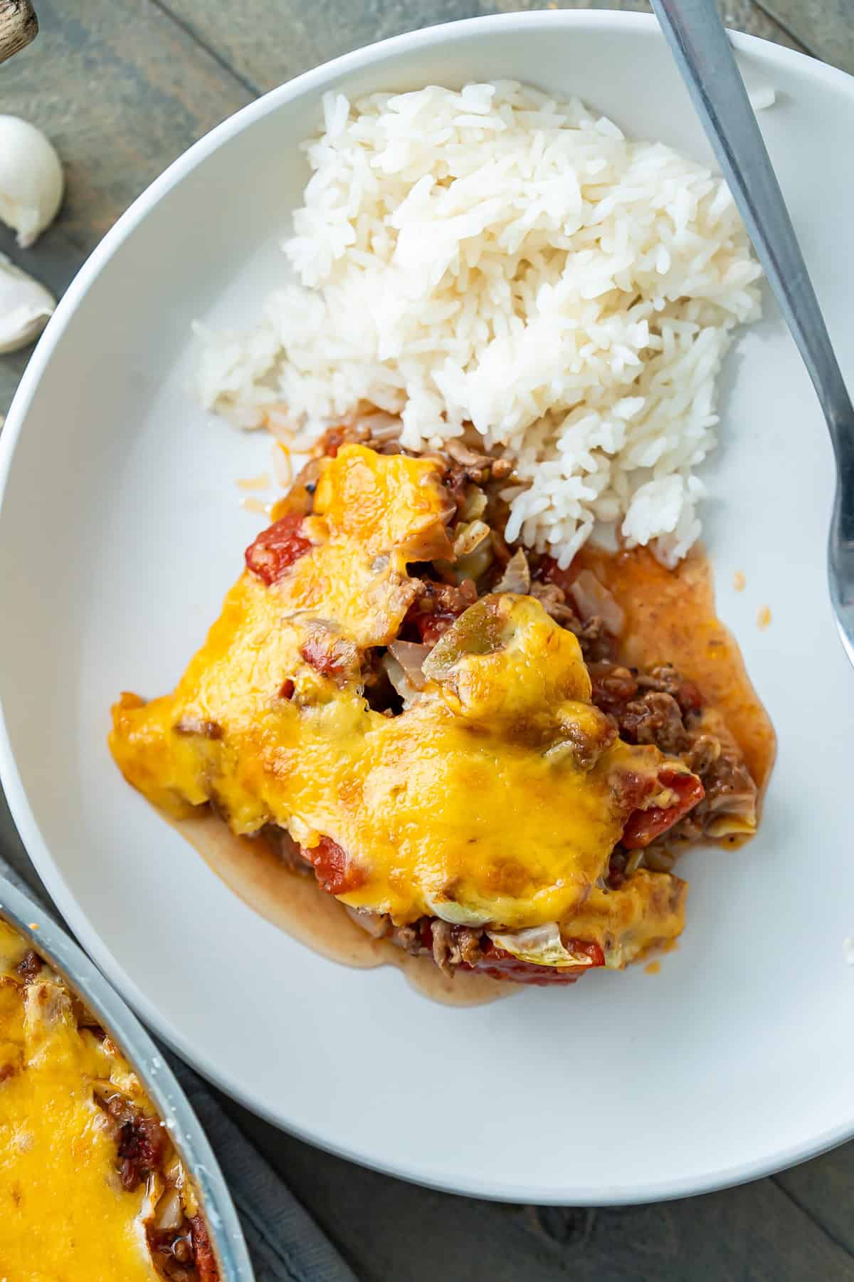 A plated scoop of cabbage roll skillet with bubbly cheese on top and white rice on the side.